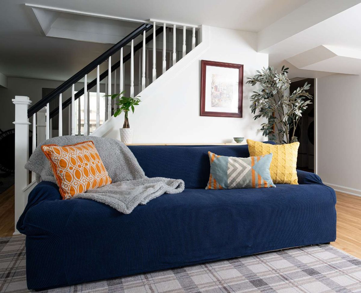 Colorful living room with navy couch, geometric pillows, and a staircase with black-and-white railings. | G&amp;L and Sons Renovations